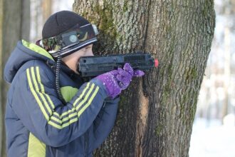 Юный боец LASERWAR за стволом дерева в зимнем лесу