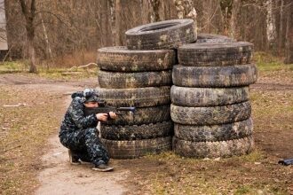 Игрок LASERWAR в камуфляже целится из-за шин.